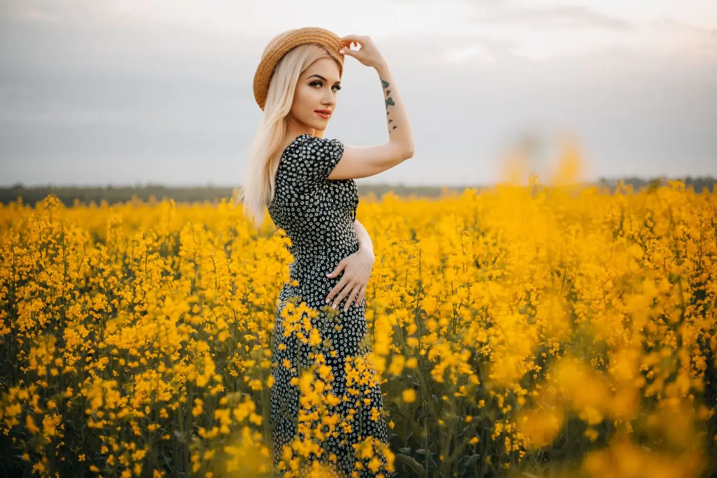 Woman in a hat standing in a yellow canola field under a blue sky