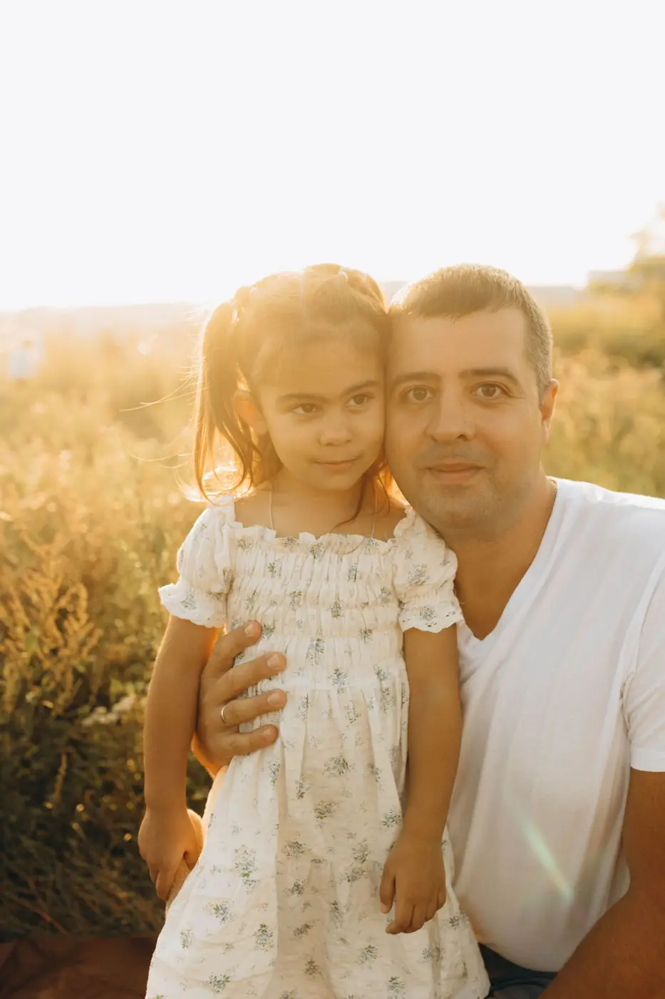Father holding his young daughter in a sunny field