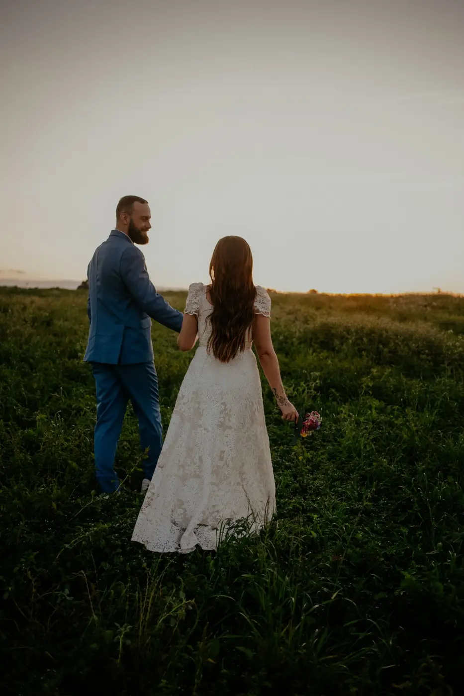 Couple walking hand in hand through a field at dusk
